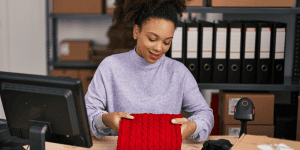 woman entrepreneur packing red sweater order at her workspace - practical example of how to start a side hustle in e-commerce or clothing resale from home