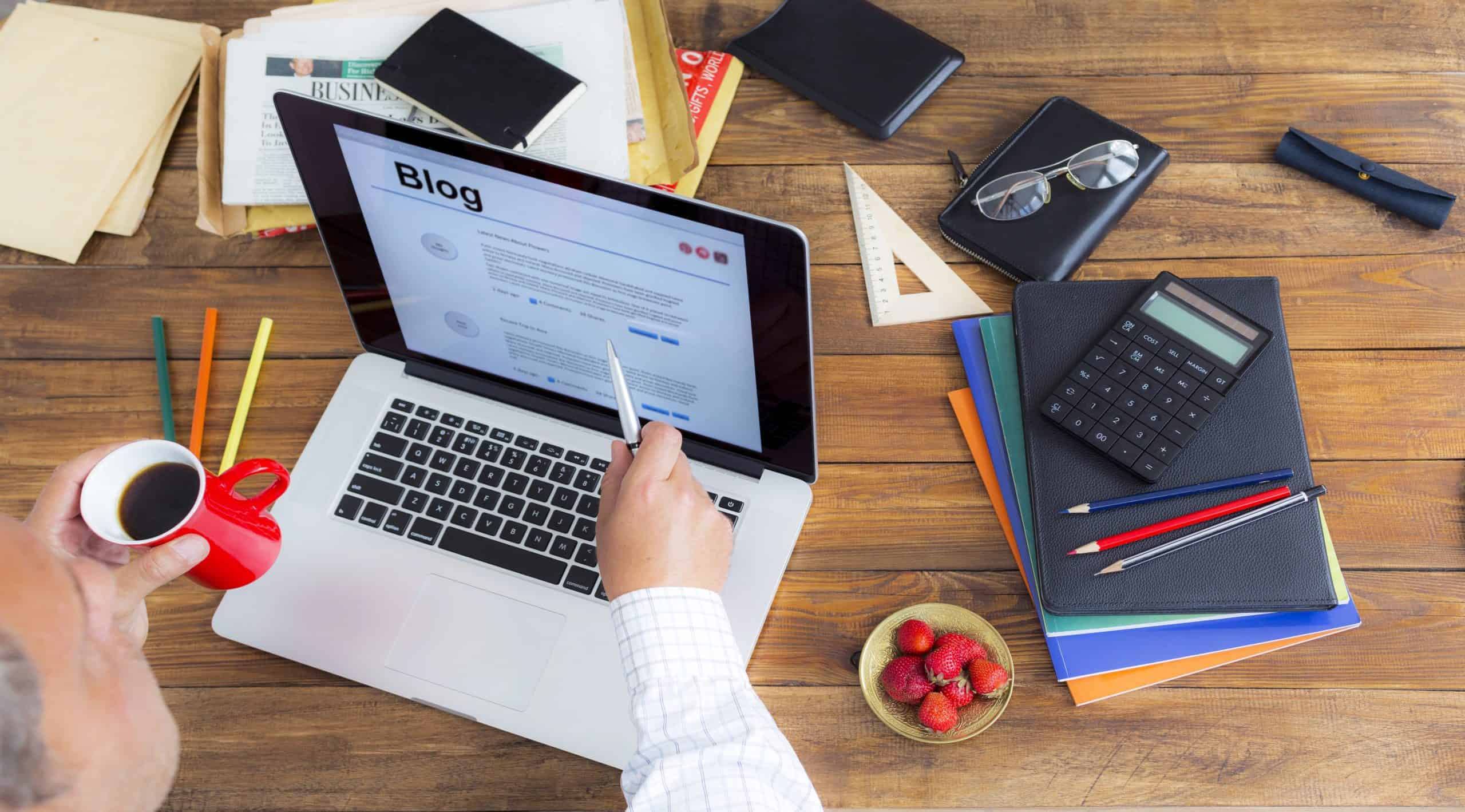 Man writing a blog on laptop on wooden desk