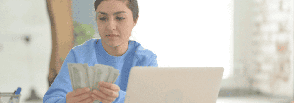 Teen Holding and Counting Money with laptop - Teen Money Mistakes