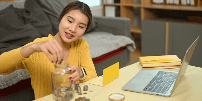 Teen girl putting coins in jars on the living room coffee table - talking to teens about money