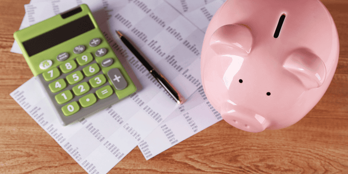 Green calculator black pen budgeting sheets pink piggy bank on the table - teen banking basics