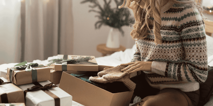 Teen sitting on her bed opening a gift - Holiday Gifts for Money Skills 