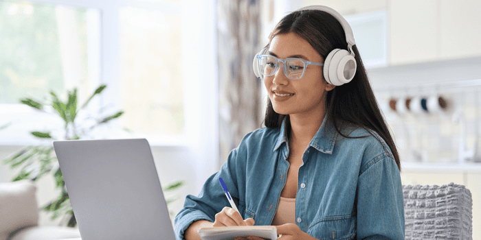 Teen girl with white headphones writing on notebook - Money Tracker Notebooks for Teens