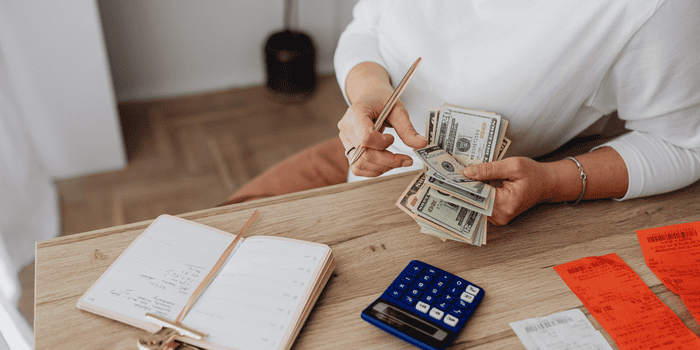 Woman counting US cash with journal and calculator on table - Financial Journals for High Schoolers
