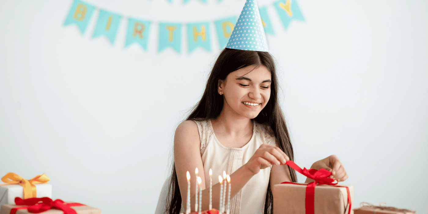Teen girl standing in front of her birthday gift table and opening her gifts. Birthday Gift Ideas for Teen Girls